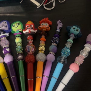 May include: A set of ten colorful pens decorated with beads and characters from the movie Inside Out. Each pen features a different character, including Joy, Sadness, Anger, Fear, and Disgust. The pens are perfect for adding a touch of personality to your writing.