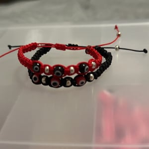 May include: Two red and black string bracelets with silver beads and blue evil eye charms.