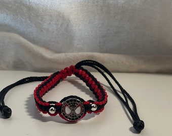 Könnte beinhalten: Ein geflochtenes Armband in Rot und Schwarz mit einem silbernen Anhänger mit dem Spider-Man-Logo.