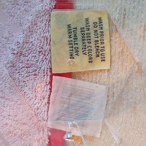 May include: A yellow care label with instructions for washing and drying a garment. The label says "Wash prior to use, Do not bleach, Wash deep colors separately, Tumble dry warm setting."