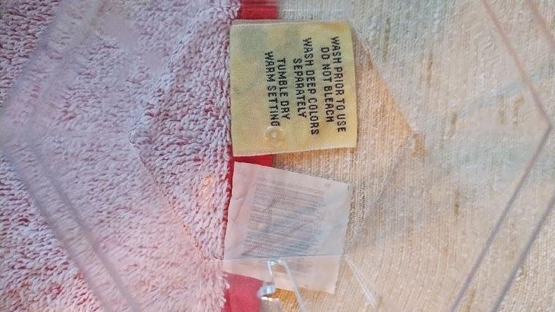 May include: A yellow care label with instructions for washing and drying a garment. The label says "Wash prior to use, Do not bleach, Wash deep colors separately, Tumble dry warm setting."