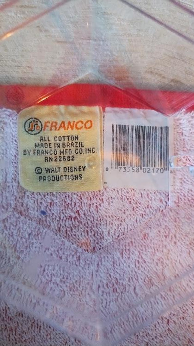 May include: A white towel with a red border and a yellow label that reads "FRANCO ALL COTTON MADE IN BRAZIL BY FRANCO MFG. CO. INC. RN22682 &copy; WALT DISNEY PRODUCTIONS" and a barcode with the number "0 73558 02170".