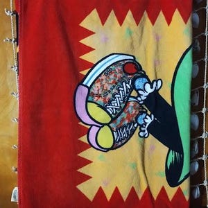 May include: Red beach towel with a yellow and red starburst design. A cartoon character with green and black clothing is wearing colorful sneakers.