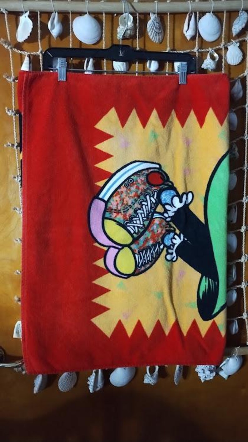 May include: Red beach towel with a yellow and red starburst design. A cartoon character with green and black clothing is wearing colorful sneakers.