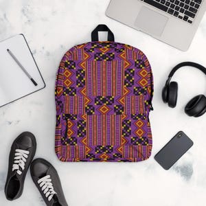 May include: A purple backpack with a geometric pattern in red, yellow, and black. The backpack is surrounded by a laptop, headphones, a smartphone, a notebook, and black sneakers.