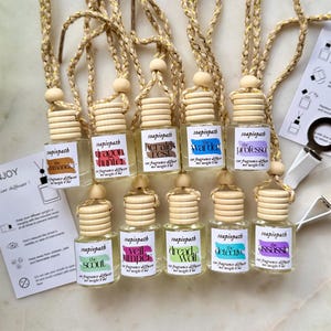 May include: Ten small glass car fragrance diffuser bottles with wooden caps and braided gold-flecked cords. Each bottle features a label with the brand name Soapiopath, a unique scent name, and a net weight of 8 ml. Two instruction cards are included.