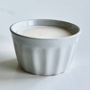 May include: A white ceramic bowl with a fluted design, filled with a creamy white substance.