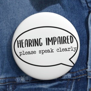 May include: White button with black text that reads "HEARING IMPAIRED please speak clearly" in a speech bubble shape.