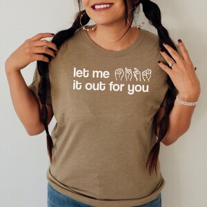 May include: A brown t-shirt with the text "let me sign it out for you" in white. The text is accompanied by a series of hand signs in white.