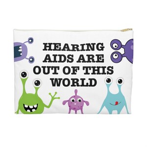 May include: White zippered pouch with the text "HEARING AIDS ARE OUT OF THIS WORLD" and cartoon alien illustrations in green, purple, and blue. The pouch has a gold zipper.