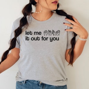 May include: Grey t-shirt with the text "let me it out for you" in black lettering. The text includes a series of hand signs in American Sign Language.