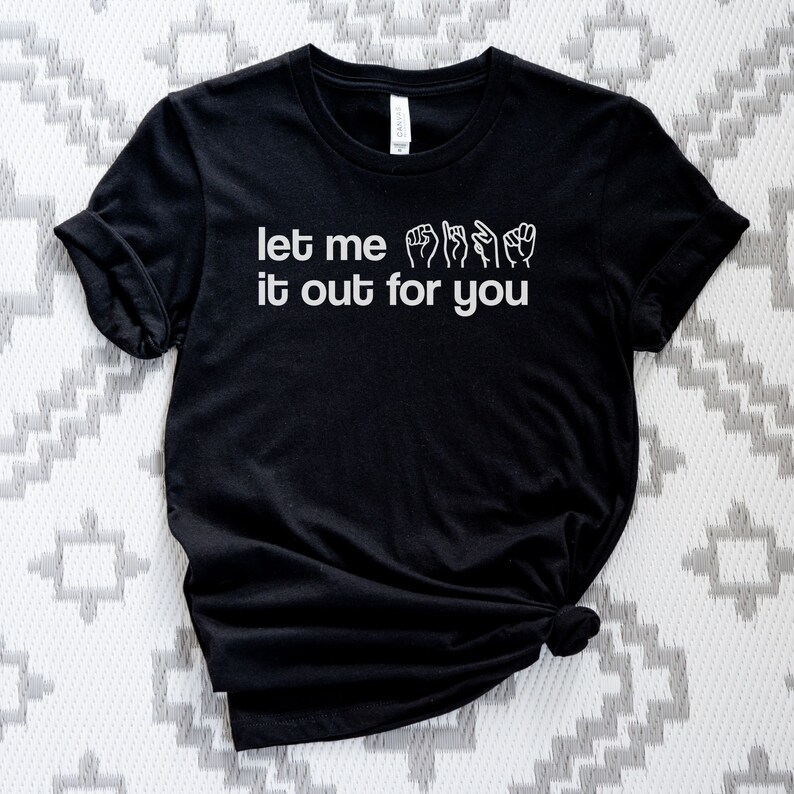May include: Black t-shirt with the text "let me it out for you" in white lettering. The text is accompanied by a series of hand signs in sign language.