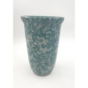 May include: A tapered vase featuring a speckled pattern of white and teal blue. The vessel has a wide, flared rim that narrows toward the base, showcasing a consistent mottled texture across the entire exterior surface of the object.