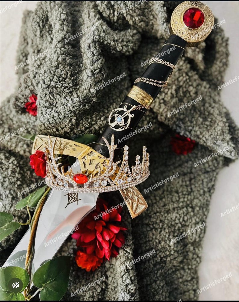 May include: A silver sword with a black handle and a gold crown with red jewels. The sword is lying on a gray fuzzy surface with red flowers.