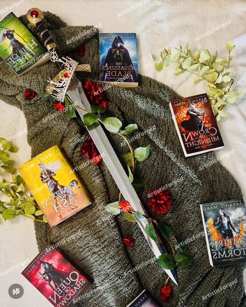 May include: A silver sword with a gold crown handle, lying on a green blanket with red roses. There are several fantasy novels with titles in a foreign language, including "The Assassin's Blade", "Crown of Midnight", "Queen of Shadows", and "Empire of Storms".