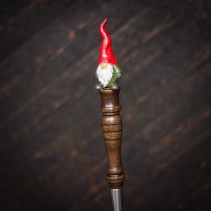 May include: A wooden beer tap handle with a gnome figurine on top. The gnome is wearing a red hat and green clothing.
