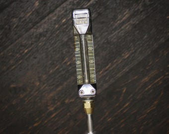 May include: A vertical CO2 flow meter featuring a clear glass tube with numerical markings from 0 to 50. The device has a metallic silver top labeled with the word FLOW and a brass-colored connector at the base attached to a silver metal rod.