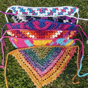 Könnte beinhalten: Eine Sammlung von sechs dreieckigen Häkel-Bandanas in verschiedenen Farbkombinationen, darunter Weiß, Pink, Blau, Schwarz, Lila, Orange, Gelb und Grün. Jedes Bandana hat an den Ecken dünne Häkelbänder zur Befestigung des Kleidungsstücks.