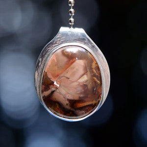 May include: A silver pendant with a brown, pink, and white agate stone. The stone is set in a silver bezel and hangs from a silver chain.