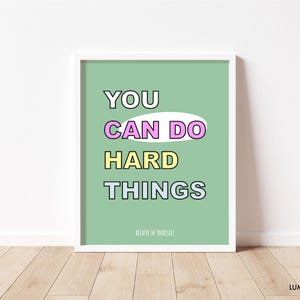 May include: A framed print with the words "YOU CAN DO HARD THINGS" in a colorful, bold font on a light green background. The text is outlined in black, with "CAN DO" in a pink oval. The phrase "BELIEVE IN YOURSELF" is at the bottom.