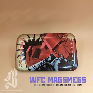 Könnte beinhalten: Holographischer rechteckiger Knopf mit einer roten und grauen Illustration eines Robotercharakters. Das Wort "MANEATER" steht in goldfarbenen Buchstaben auf der linken Seite. Der Text "WFC MAGSMEGS" und "HOLOGRAPHIC RECTANGULAR BUTTON" befindet sich unten.