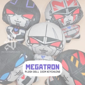 May include: Plush Megatron doll keychains. The plush toys are gray, black, and red, with a cartoon-like design. The text "MEGATRON PLUSH DOLL 10CM KEYCHAINS" is displayed on a white and purple banner.