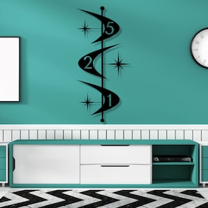 May include: Black metal wall art featuring a mid-century modern design. The art piece has a vertical orientation with curved shapes, starburst accents, and the numbers 1, 2, and 5. The art is mounted on a teal wall.