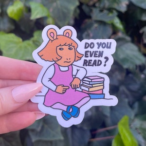 May include: A sticker featuring a cartoon girl sitting with a stack of books. The sticker has the text "Do you even read?"