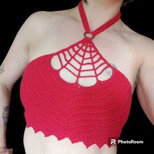 May include: Red crochet halter top with a spiderweb design. The top has a halter neck strap and a ring closure at the back of the neck.