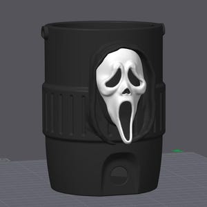 May include: A matte black cylindrical container featuring a raised, white, three-dimensional ghost mask with a hooded shroud. The exterior surface has a textured band around the middle and a small circular opening near the base of the vessel.