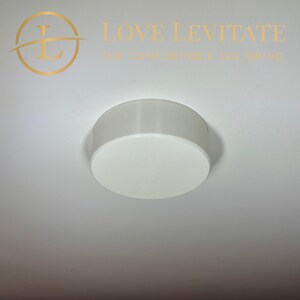 May include: White round ceiling mount for a swing. The mount is made of plastic and has a smooth surface.