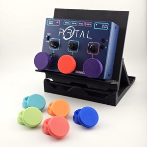 May include: A dark blue Portal audio effects pedal with three black control knobs, mounted on a black angled stand. Three colorful circular foam covers are attached to the knobs, with additional loose foam covers in blue, green, orange, and red.