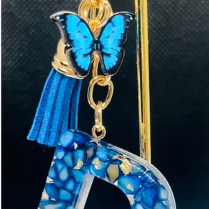 Llavero acrílico azul con inicial D, borla y dije de mariposa