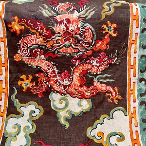 May include: A textile featuring a detailed illustration of a red and orange dragon with a brown background. The dragon is surrounded by white clouds and decorative borders in teal, orange, and white. This design is suitable for home decor.