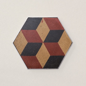 May include: A hexagonal tile with a geometric pattern of black, red, and brown squares and rectangles. The tile is framed with a silver border.