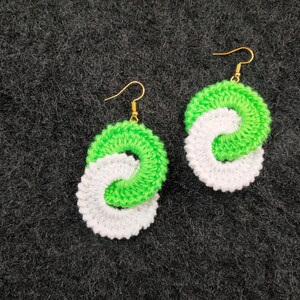 May include: A pair of crocheted earrings with a white and green swirl design. The earrings are made with a soft yarn and have gold hooks.