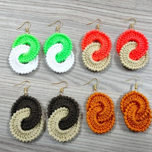 May include: Six pairs of crocheted earrings in various colors, including green, white, orange, and brown. Each earring is a double-loop design.