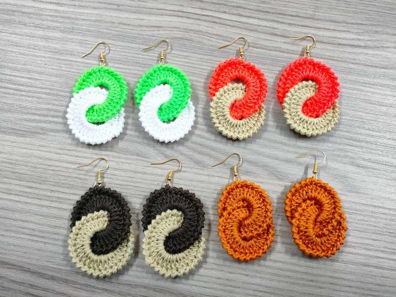 May include: Six pairs of crocheted earrings in various colors, including green, white, orange, and brown. Each earring is a double-loop design.