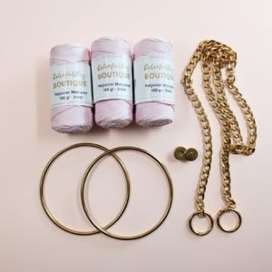 May include: Three spools of light pink polyester macrame cord labeled Colorful Bag Boutique 100 gr 3mm, two gold metal circular rings, two small gold circular fasteners, and a long gold metal chain with two attached circular rings at the ends.