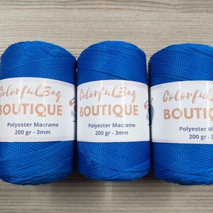 May include: Three spools of vibrant blue polyester macrame cord, each wrapped in a white paper label featuring the text Colorful Bag BOUTIQUE, Polyester Macrame, 200 gr - 3mm. The cord has a smooth, braided texture and a consistent bright blue color.