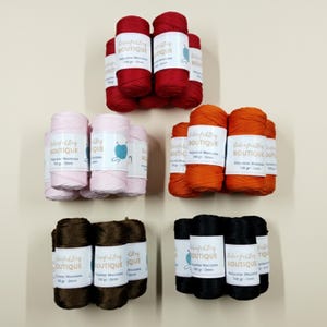 May include: Five bundles of polyester macrame cord in red, light pink, orange, dark brown, and black. Each bundle features a white label with the text Colorful Bag Boutique, 100 gr, and 2mm. The cord is wound into cylindrical spools for crafting.