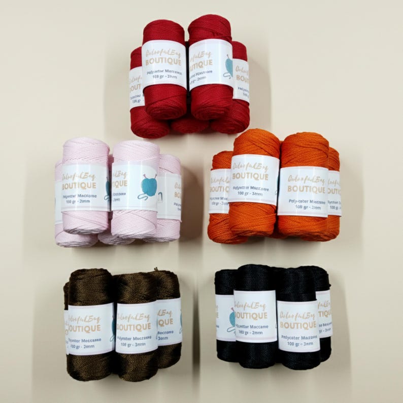 May include: Five bundles of polyester macrame cord in red, light pink, orange, dark brown, and black. Each bundle features a white label with the text Colorful Bag Boutique, 100 gr, and 2mm. The cord is wound into cylindrical spools for crafting.