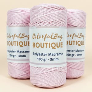 May include: Three spools of light pink polyester macrame cord. Each spool features a white paper label with the text ColorfulBag BOUTIQUE, Polyester Macrame, 100 gr - 3mm. The cord has a braided texture and is wound tightly into a cylindrical shape.