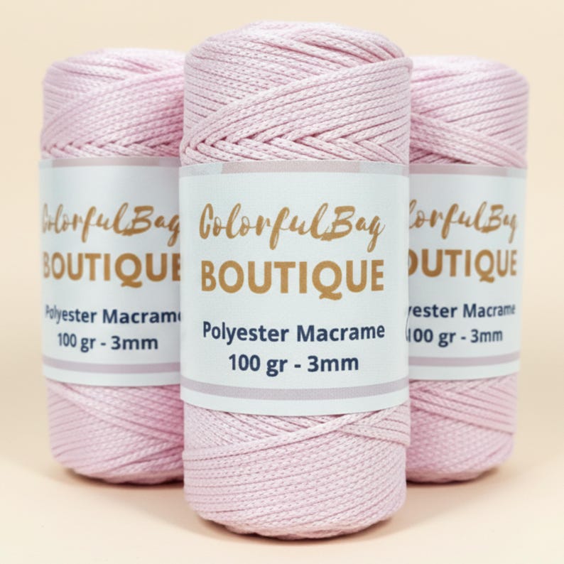 May include: Three spools of light pink polyester macrame cord. Each spool features a white paper label with the text ColorfulBag BOUTIQUE, Polyester Macrame, 100 gr - 3mm. The cord has a braided texture and is wound tightly into a cylindrical shape.