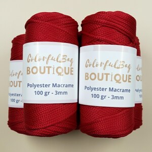 May include: Four spools of deep red polyester macrame cord arranged together. Each spool features a white paper label with the text ColorfulBag BOUTIQUE, Polyester Macrame, 100 gr - 3mm printed in dark blue and gold lettering on the front.