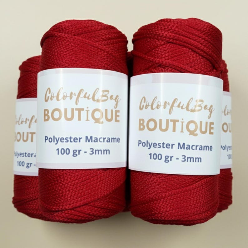 May include: Four spools of deep red polyester macrame cord arranged together. Each spool features a white paper label with the text ColorfulBag BOUTIQUE, Polyester Macrame, 100 gr - 3mm printed in dark blue and gold lettering on the front.