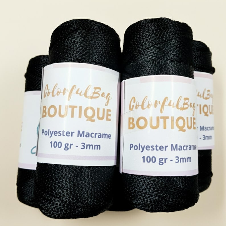 May include: Several spools of black polyester macrame cord, each wrapped in a white paper label featuring the text Colorful Bag BOUTIQUE, Polyester Macrame, 100 gr - 3mm. The cord has a smooth, braided texture and a consistent dark black color.