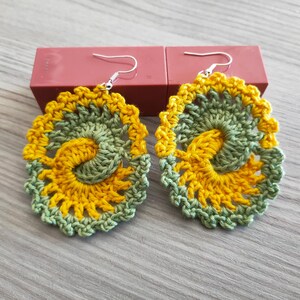 May include: A pair of crocheted earrings with a yellow and green swirl design.