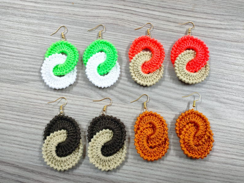 May include: Six pairs of crocheted earrings in various colors, including green, white, orange, and brown. Each earring is a double-loop design.