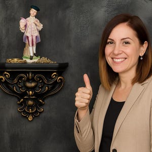 May include: A decorative black wall shelf with gold accents supports a figurine of a man in historical attire. A woman in a tan blazer gives a thumbs-up. The background is a dark gray textured wall.